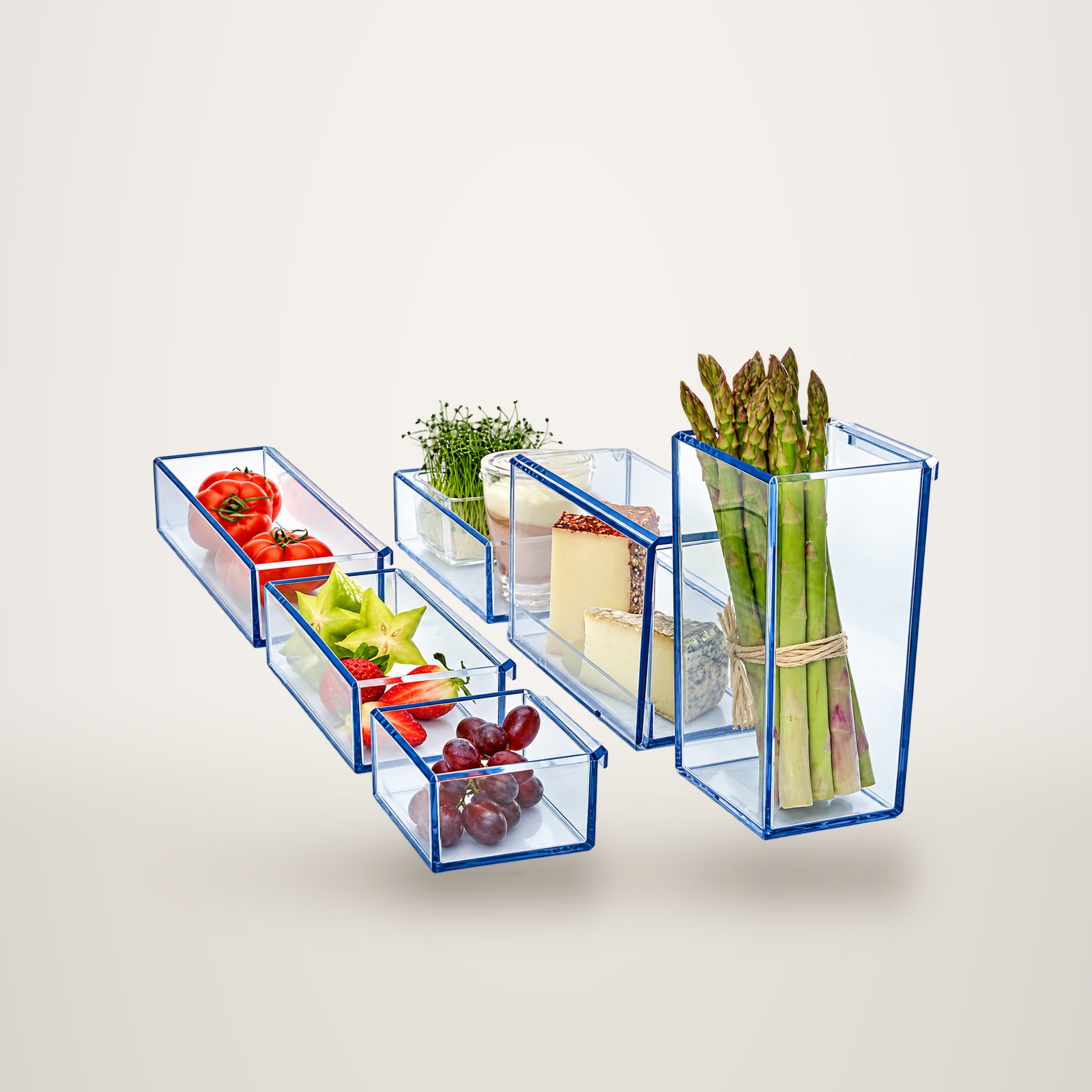 Several clear glass trays with blue-tinted edges holding tomatoes, fruit, grapes, cheeses, sprouts and asparagus.