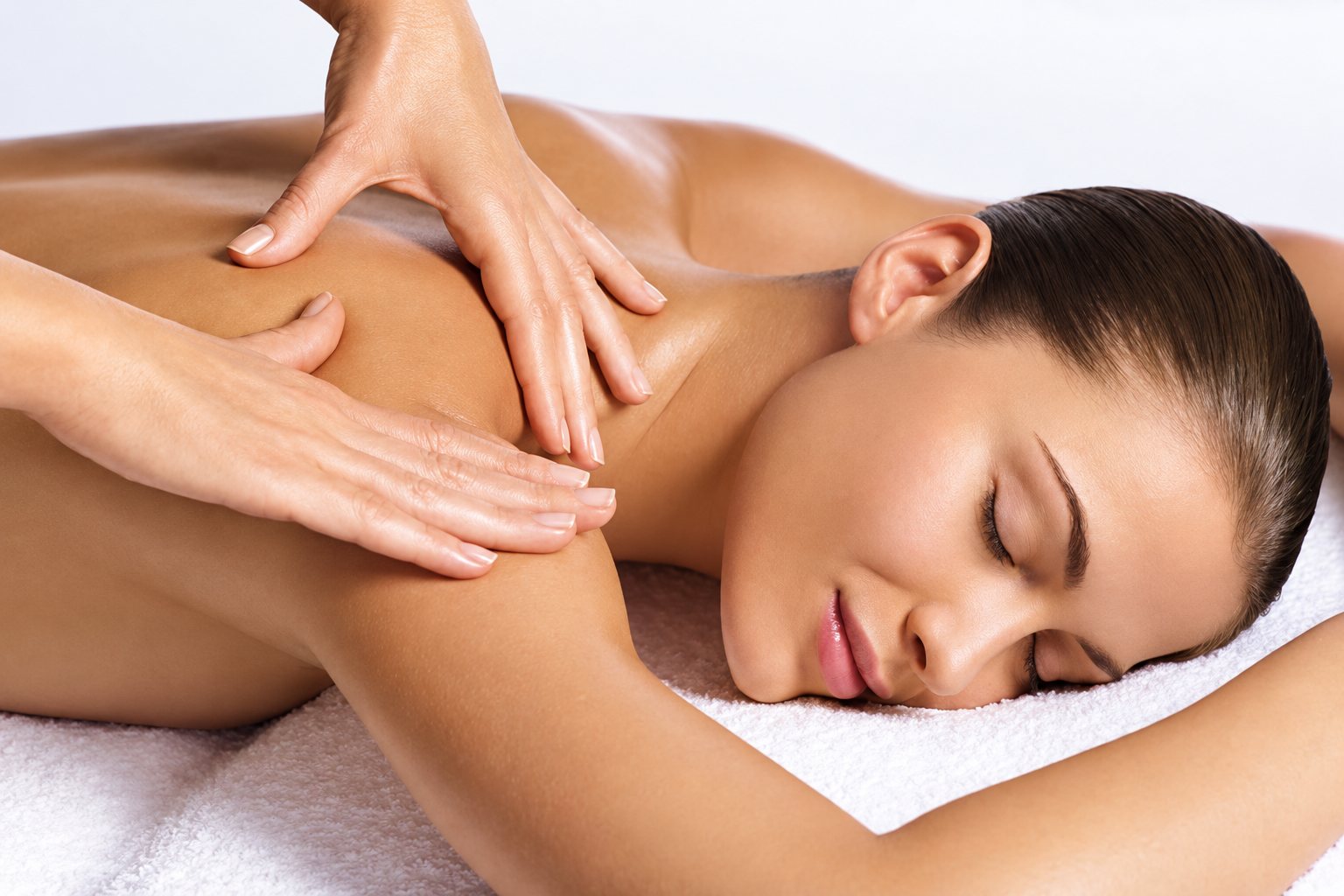Une femme les yeux fermés, allongée sur une serviette blanche, reçoit un massage du dos et des épaules par deux mains.
