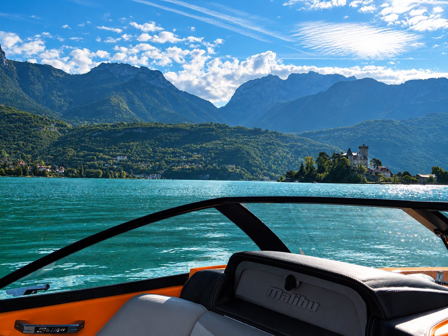 Vue depuis le poste de pilotage d'un bateau Malibu sur un lac turquoise, avec un château au bord de l'eau et des montagnes en arrière-plan.